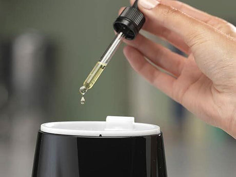 Person adding essential oil drop to a black Dimplex aroma diffuser with white top