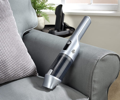 Silver Dirt Devil handheld vacuum resting on a gray fabric couch with a textured pillow nearby