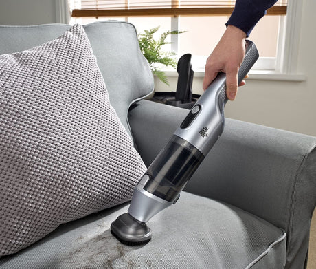 Dirt Devil handheld vacuum cleaning dirt from a gray fabric sofa with textured pillow