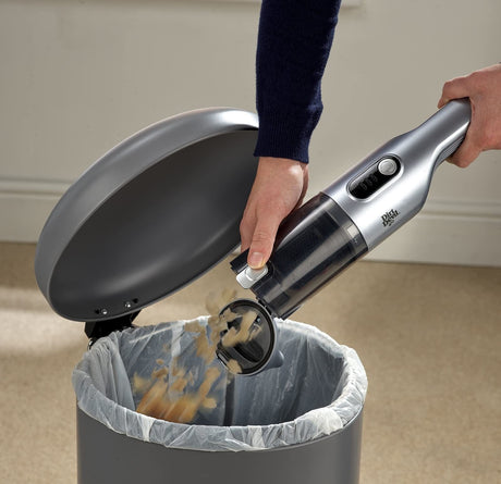Person emptying dirt and debris from Dirt Devil handheld vacuum into a trash can