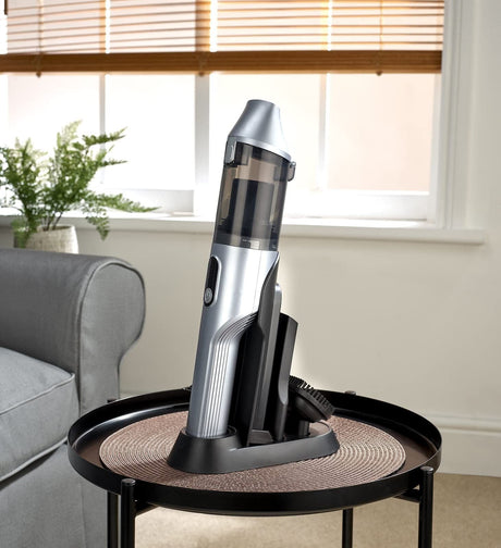 Silver Dirt Devil handheld vacuum with charging dock on a round table in a living room