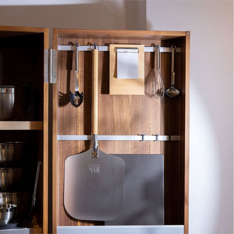 Rectangular pizza stone for oven and metal pizza peel hanging inside a wooden kitchen cabinet