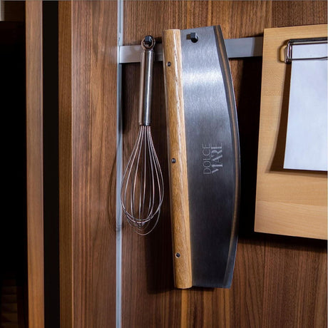 Dolce Mare stainless steel pizza cutter hanging on kitchen wall with whisk and wooden board
