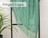 Green loose weave throw blanket with fringed edges hanging on a black ladder next to a green plant