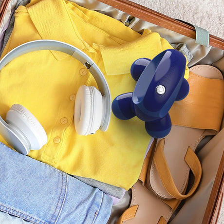 Homedics Quattro Mini Massager in blue placed inside a suitcase with yellow shirt headphones and sandals