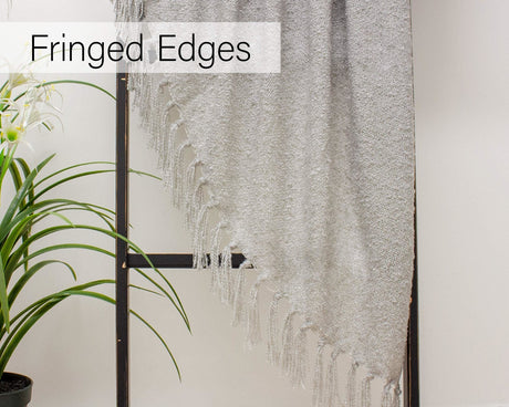 Light grey fringed throw blanket hanging on a black rack with a green plant nearby