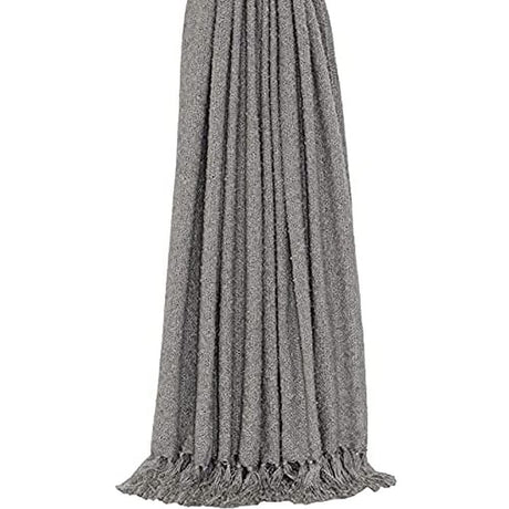 Light grey fringed throw blanket made of soft textured fabric hanging with detailed tassel edges