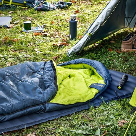 Lightweight sleeping bag for hiking with blue exterior and green interior laid out on grass near a tent