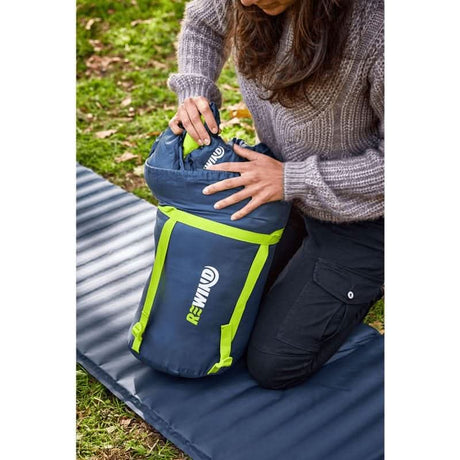Person packing a lightweight sleeping bag for hiking from CLICKK Home Store into a blue and green compression sack outdoors