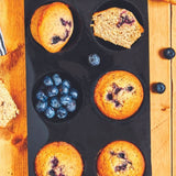 Premium baking accessories set featuring blueberry muffins in a black non-stick baking tray by Magimix x De Buyer
