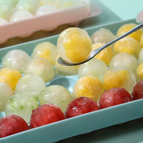 Mini sphere ice cube tray with colorful frozen fruit ice spheres being scooped with a spoon