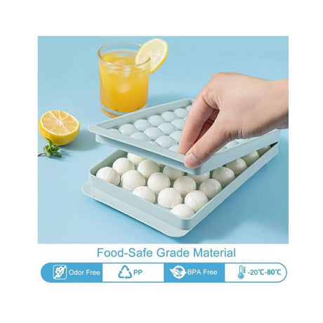 Hand holding mini sphere ice cube tray with round ice balls and a glass of orange juice with lemon