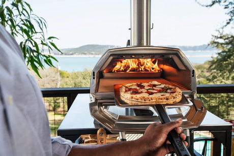 Person using a 14 inch pizza peel to remove a freshly baked pizza from an outdoor pizza oven