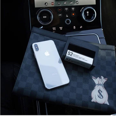CLICKK Home Store medium hold hair gel box next to a silver smartphone on a checkered black pouch inside a car