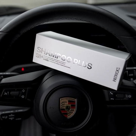 Patrick's thickening shampoo in white box packaging placed on a Porsche car steering wheel
