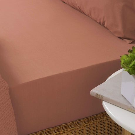 Red clay fitted sheet single on a bed with matching pillow and bedside table with plant