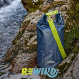 Blue dry bag 22L with green strap placed on wet rocks beside flowing river water