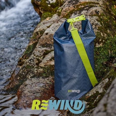 Blue dry bag 22L with green strap placed on wet rocks beside flowing river water