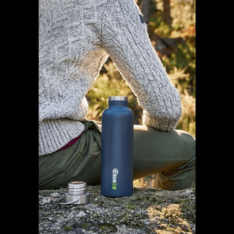 Person sitting outdoors with an eco-friendly water bottle in dark blue color, perfect for eco-conscious lifestyles