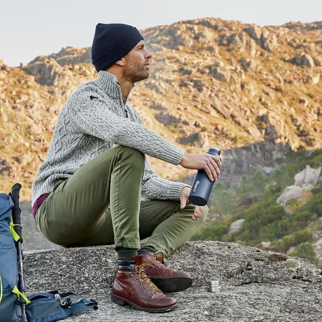 Man sitting on a rock with a CLICKK eco-friendly water bottle while enjoying nature outdoors