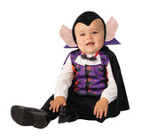 Toddler wearing a toddler vampire costume with large ears, purple vest, and black cape sitting smiling