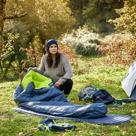 Woman setting up a self inflating camping mat and sleeping bag outdoors during a camping trip