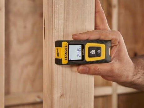 Stanley laser distance measurer held against wooden beam measuring 24.45 feet in construction setting