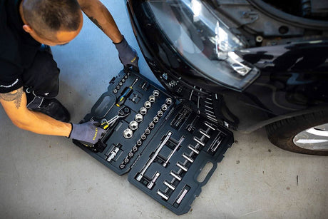 Mechanic using a Stanley socket set 72 tooth in a Black and Decker case beside a car tire
