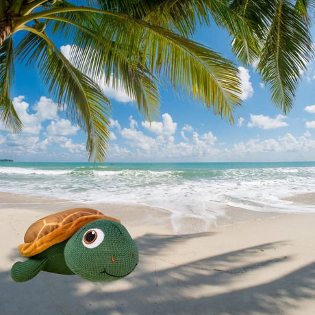 Taylor the Turtle plush toy on a sandy beach under palm trees with ocean waves in the background