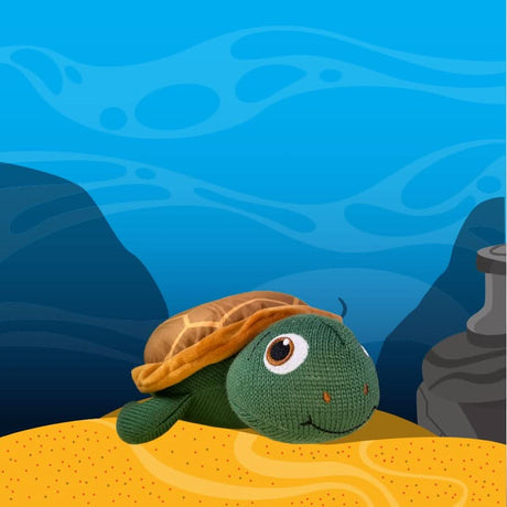 Taylor the Turtle plush toy on sand with underwater ocean background and rocks