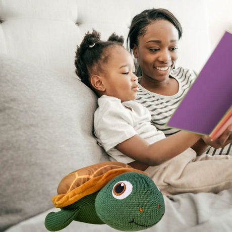 Taylor the Turtle plush toy next to child and mother reading a book on a couch