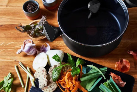 Black Tefal induction pot 24cm with fresh vegetables and herbs on wooden kitchen table