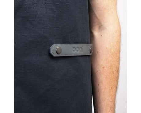 Close-up of heavy duty canvas apron in dark color with leather strap detail and metal buttons