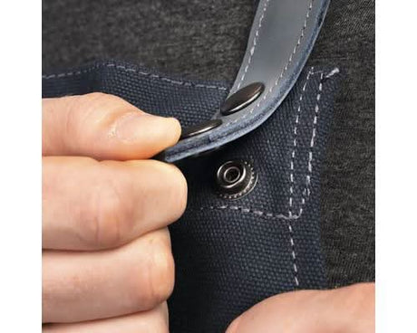 Close-up of a hand fastening snap button on a heavy duty canvas apron strap with reinforced stitching