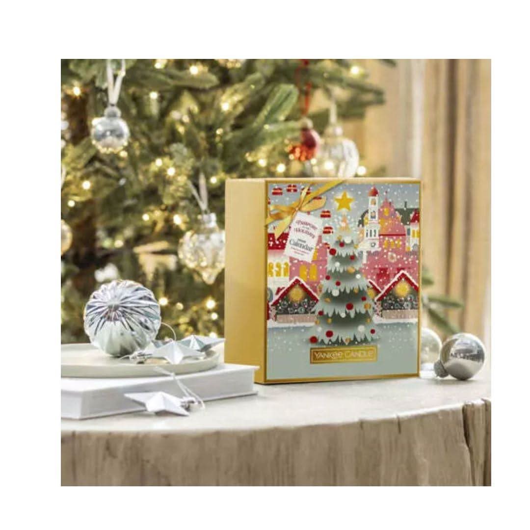 Festive Yankee Candle advent calendar with holiday village design and Christmas tree on table near decorated tree
