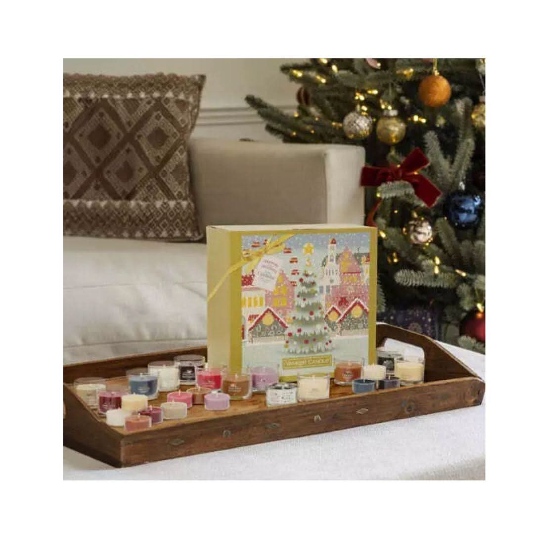 Yankee Candle advent calendar with assorted scented candles displayed on a wooden tray near Christmas tree